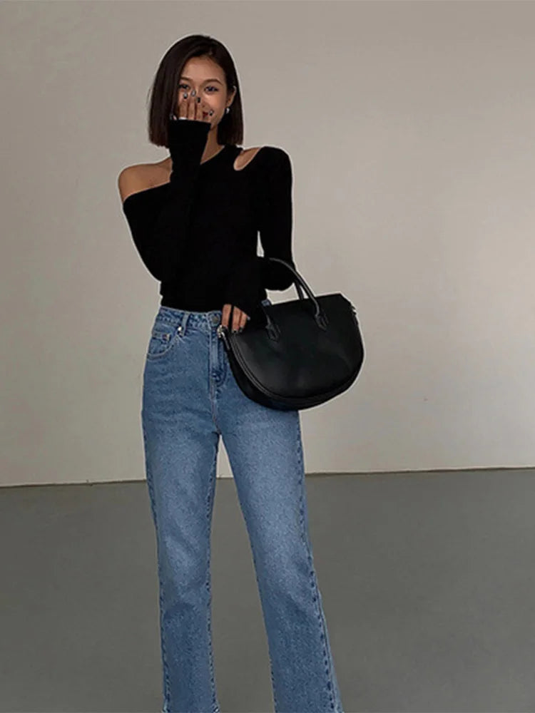 Model wearing the black asymmetric off-shoulder top while playfully covering her face, emphasizing a chic and playful style.
