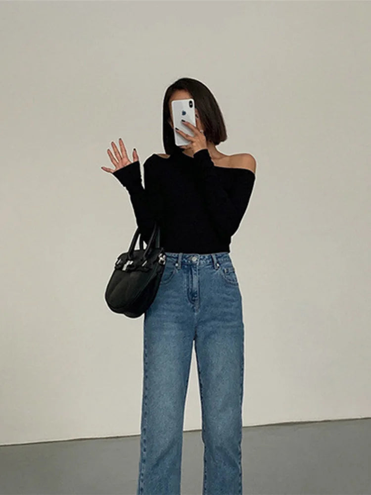 Model wearing the black asymmetric off-shoulder top while taking a selfie, showcasing a casual, chic look.