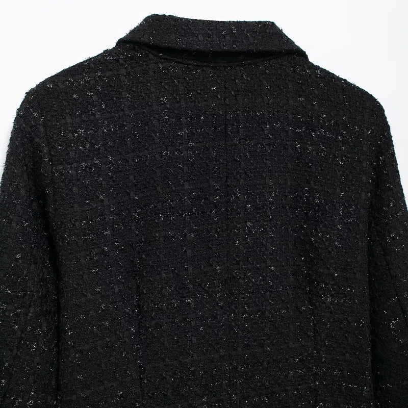 Close-up of the black tweed mini dress, highlighting its elegant bow-shaped buttons and textured fabric.