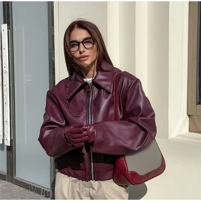 Model crossing hands in a burgundy faux leather jacket, displaying a confident and casual look.