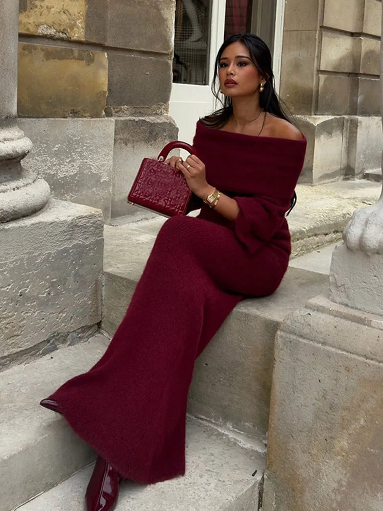 Model seated, crossing legs while wearing Burgundy off-shoulder knitted maxi dress.