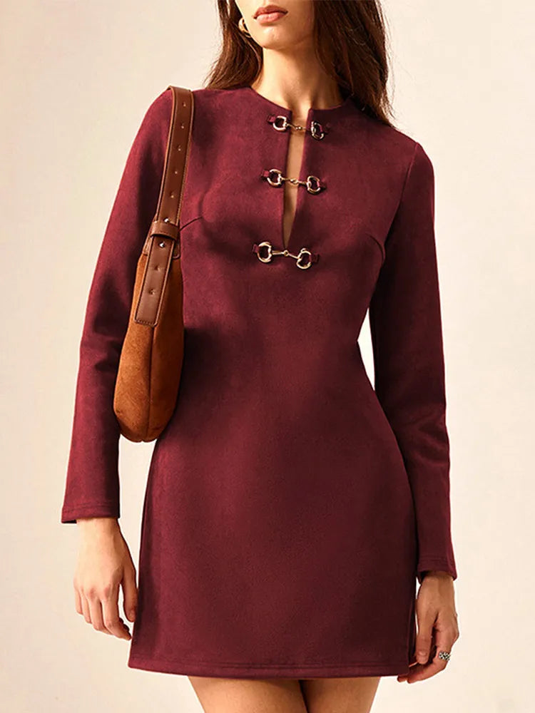 A woman wearing a burgundy mini dress with hollow out button details and a round neckline, with a back zipper closure and gold hardware.