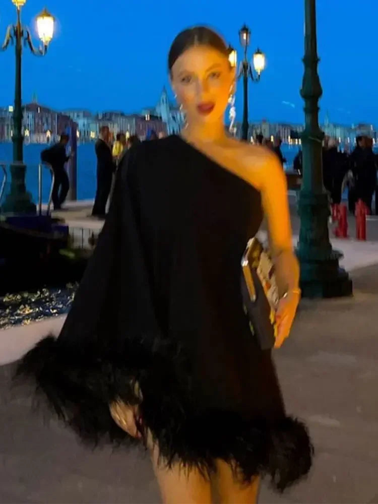 Elegant black one-shoulder mini dress with dramatic feather details for a bold fashion statement