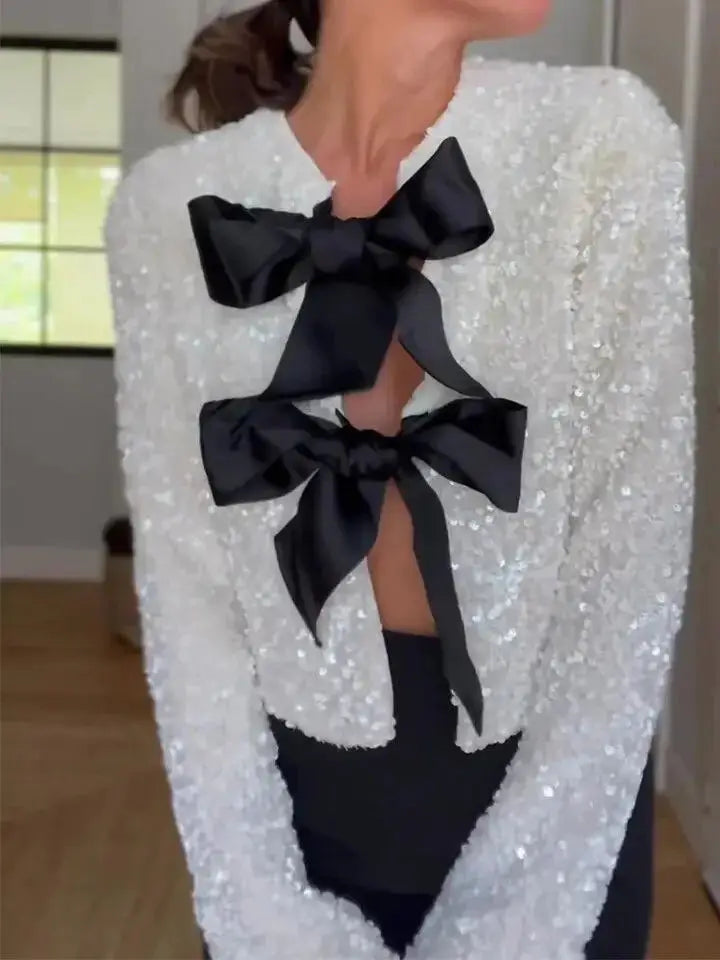 Detailed view of ivory sequined jacket, highlighting intricate bow accents and shimmering fabric.