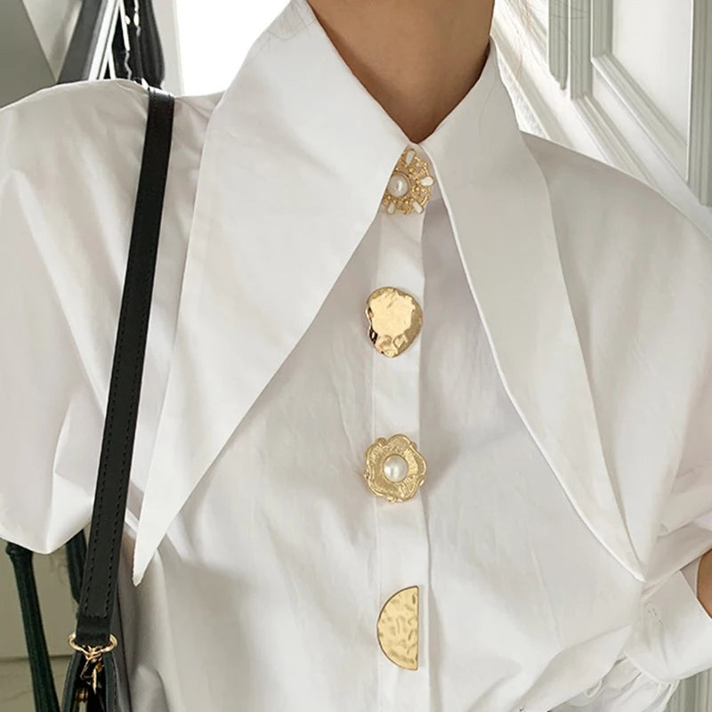 White blouse with gold pearl buttons and long collar, perfect for a polished, trendy look.